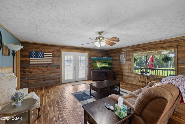 living room featuring ceiling fan, french doors, hardwood / wood-style floors, a textured ceiling, and wood walls