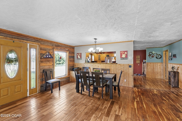 dining area featuring hardwood / wood-style floors, a textured ceiling, wooden walls, ornamental molding, and a chandelier