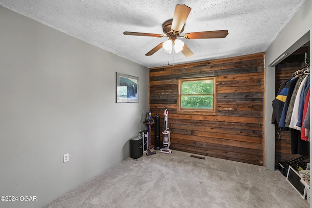 interior space featuring wood walls, a closet, ceiling fan, and a textured ceiling