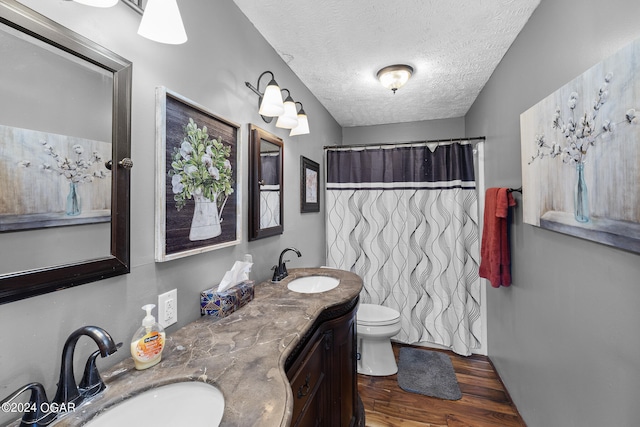 bathroom featuring dual sinks, toilet, hardwood / wood-style flooring, large vanity, and a textured ceiling