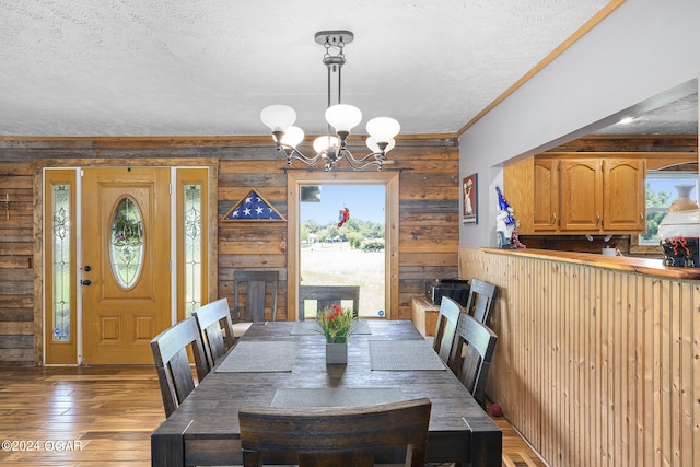 dining room with a notable chandelier, crown molding, hardwood / wood-style floors, wooden walls, and a textured ceiling