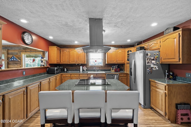 kitchen with a kitchen island, island range hood, light wood-type flooring, appliances with stainless steel finishes, and a textured ceiling