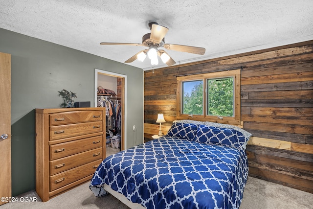 carpeted bedroom with a closet, wood walls, ceiling fan, a spacious closet, and a textured ceiling