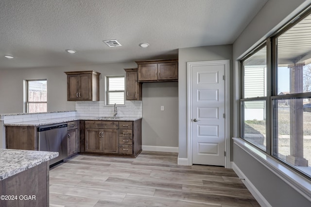 kitchen featuring sink, stainless steel dishwasher, light wood-type flooring, tasteful backsplash, and light stone counters