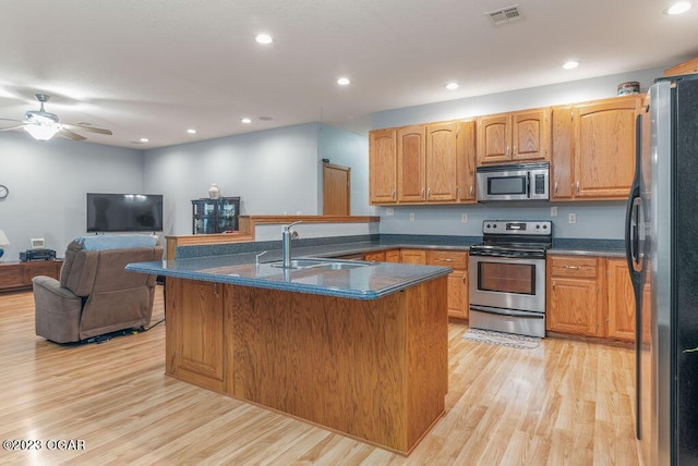 kitchen featuring a center island with sink, ceiling fan, appliances with stainless steel finishes, light hardwood / wood-style flooring, and sink