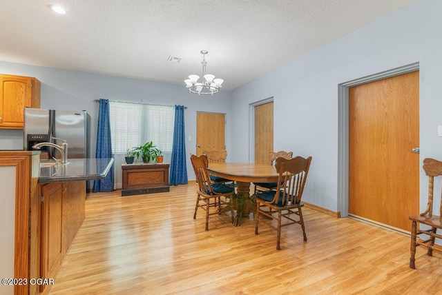 dining area featuring light wood-type flooring, a chandelier, a textured ceiling, and sink