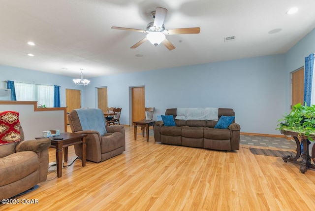 living room with ceiling fan with notable chandelier and light hardwood / wood-style floors