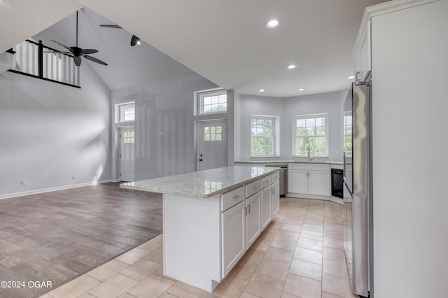 kitchen featuring a kitchen island, light tile patterned floors, stainless steel appliances, white cabinets, and light stone counters