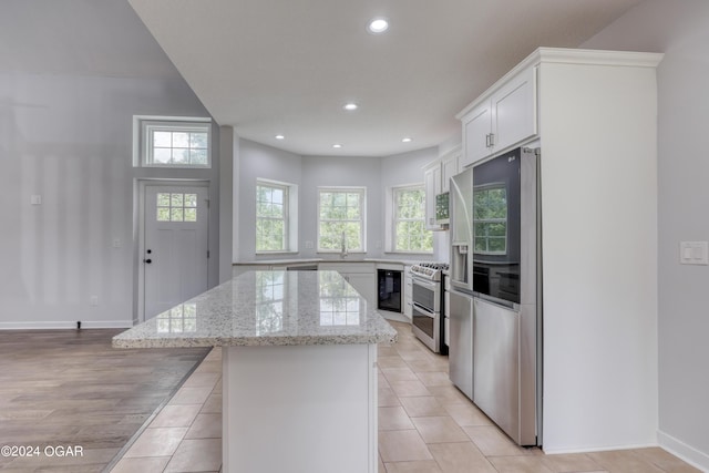 kitchen with a kitchen island, sink, white cabinetry, appliances with stainless steel finishes, and light stone counters