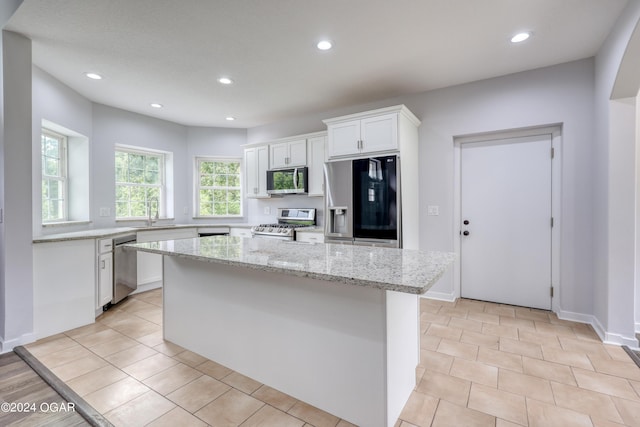 kitchen with light tile patterned floors, stainless steel appliances, light stone countertops, a kitchen island, and white cabinets