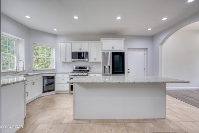 kitchen with light stone countertops, appliances with stainless steel finishes, white cabinetry, and a center island