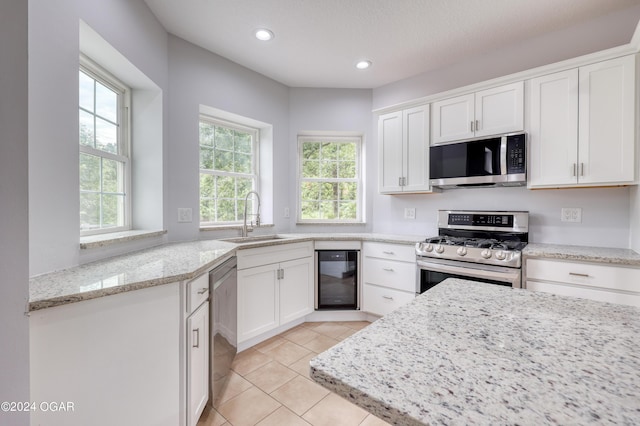 kitchen with beverage cooler, white cabinets, stainless steel appliances, sink, and light stone counters