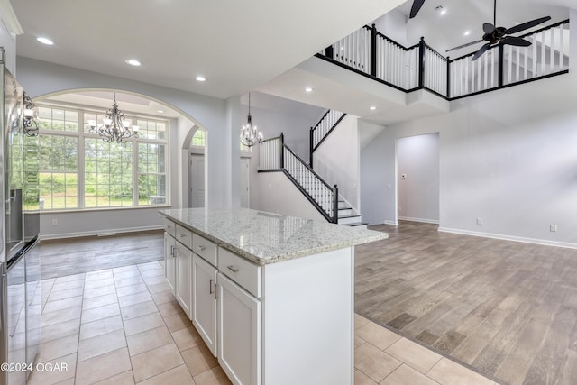 kitchen featuring light stone countertops, ceiling fan with notable chandelier, white cabinets, and a center island