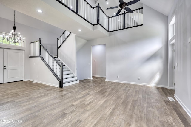 unfurnished living room with ceiling fan with notable chandelier, a towering ceiling, and light wood-type flooring