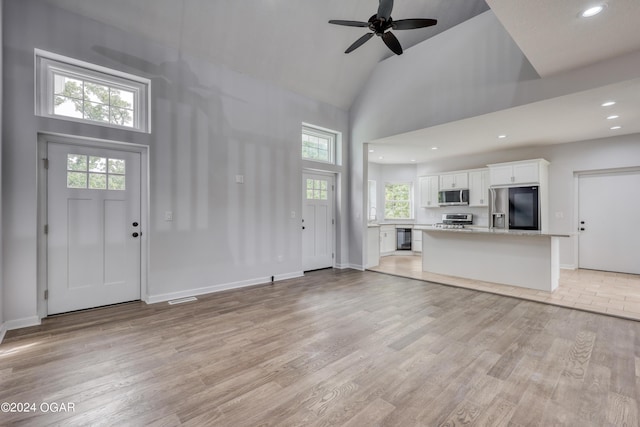 unfurnished living room featuring high vaulted ceiling, ceiling fan, plenty of natural light, and light hardwood / wood-style flooring