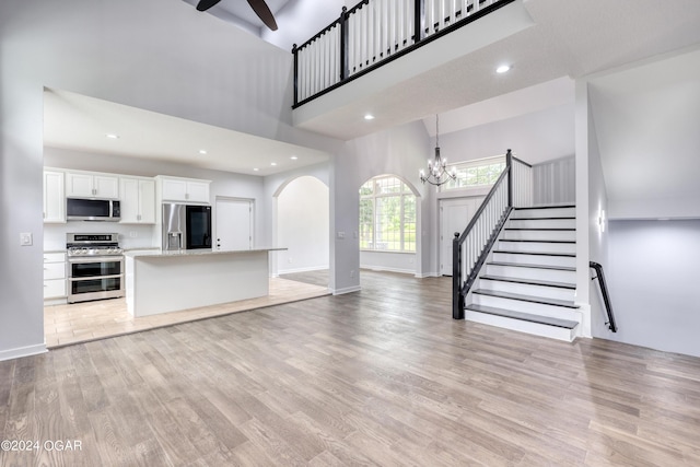 unfurnished living room featuring light hardwood / wood-style floors, a towering ceiling, and ceiling fan with notable chandelier