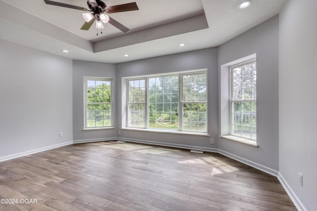 spare room with a raised ceiling, wood-type flooring, a textured ceiling, and ceiling fan