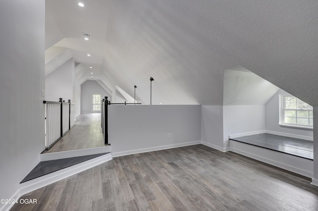 additional living space featuring vaulted ceiling, a wealth of natural light, a textured ceiling, and light hardwood / wood-style floors