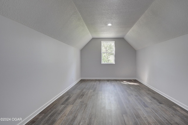 additional living space with vaulted ceiling, dark hardwood / wood-style flooring, and a textured ceiling