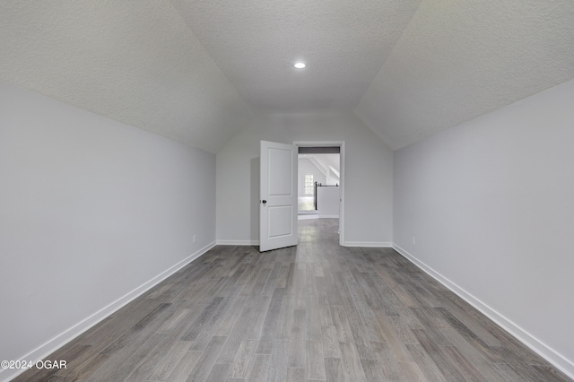 bonus room with light wood-type flooring, vaulted ceiling, and a textured ceiling