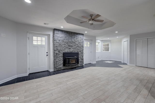 unfurnished living room with ceiling fan, a wood stove, and a tray ceiling