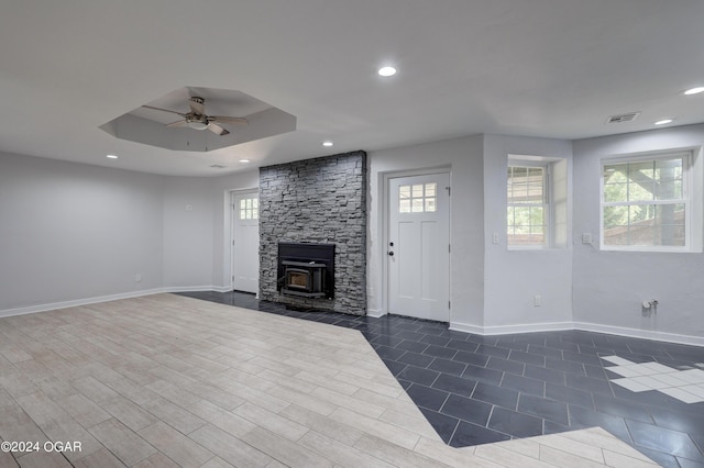 living room with ceiling fan, a wood stove, and a tray ceiling