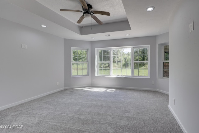 empty room with a textured ceiling, ceiling fan, carpet flooring, and a raised ceiling