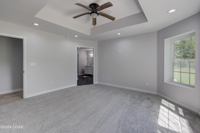 unfurnished bedroom featuring ceiling fan, ensuite bathroom, a tray ceiling, and light carpet