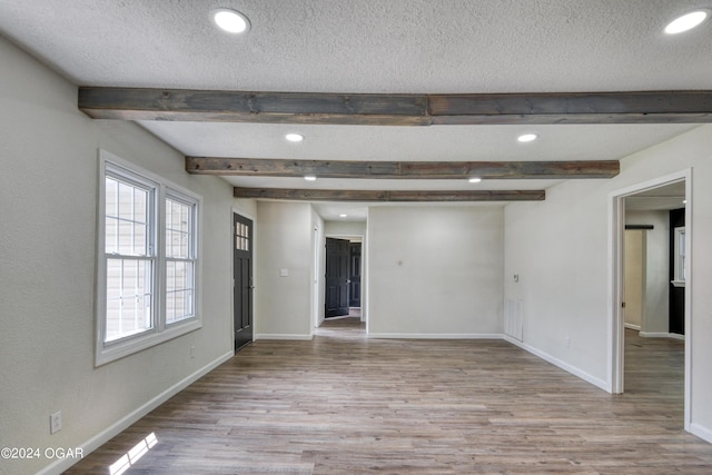 spare room featuring beam ceiling, light hardwood / wood-style floors, and a textured ceiling