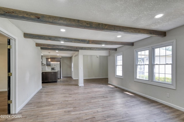 unfurnished living room featuring beam ceiling, a textured ceiling, and light hardwood / wood-style flooring