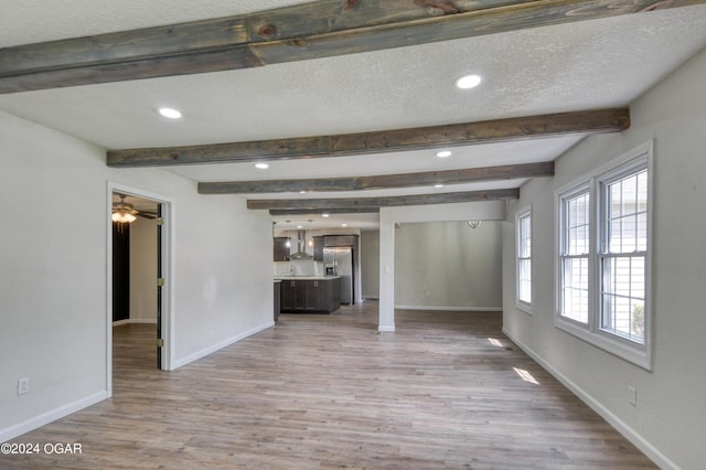 unfurnished living room featuring beam ceiling, a textured ceiling, and light wood-type flooring