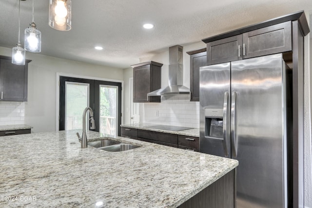 kitchen featuring stainless steel refrigerator with ice dispenser, black electric stovetop, sink, wall chimney range hood, and decorative light fixtures