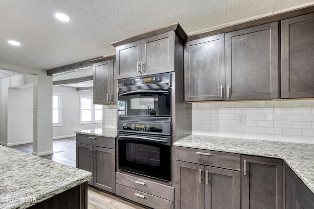 kitchen featuring light wood-type flooring, light stone countertops, double oven, tasteful backsplash, and dark brown cabinets