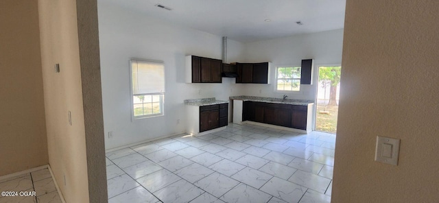 kitchen featuring light stone counters, dark brown cabinetry, sink, and light tile patterned floors