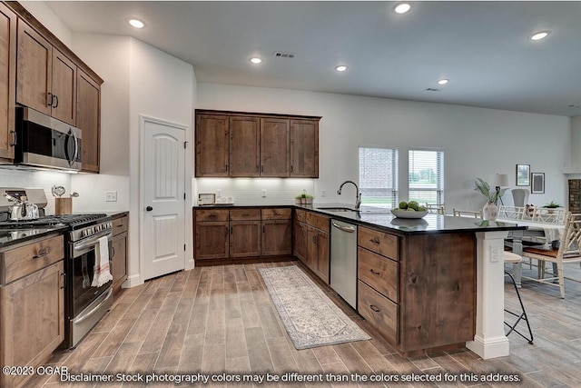 kitchen featuring sink, a kitchen breakfast bar, stainless steel appliances, light hardwood / wood-style floors, and backsplash