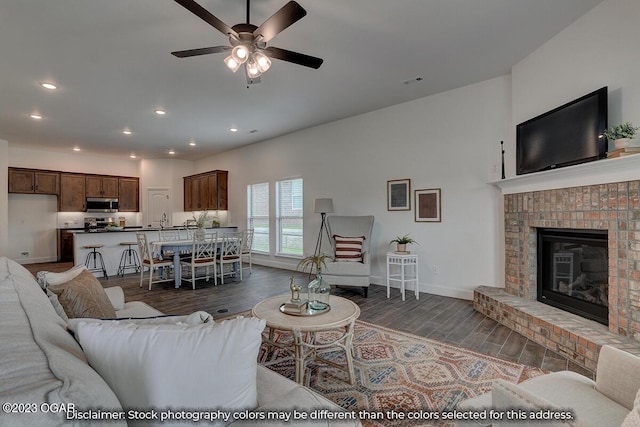 living room featuring ceiling fan, a fireplace, dark hardwood / wood-style floors, and sink