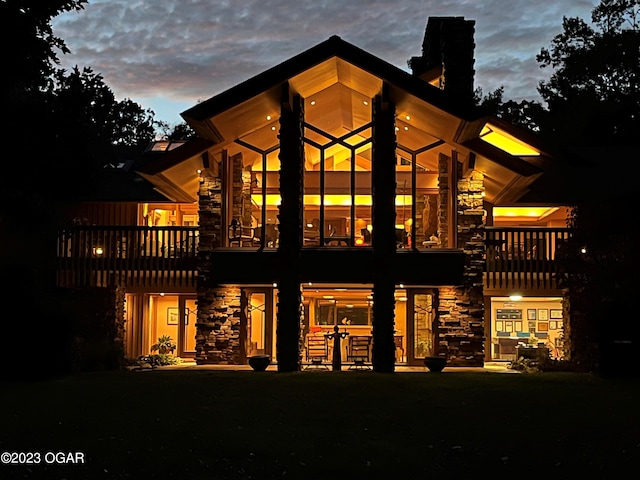 back of house at dusk with stone siding and a balcony