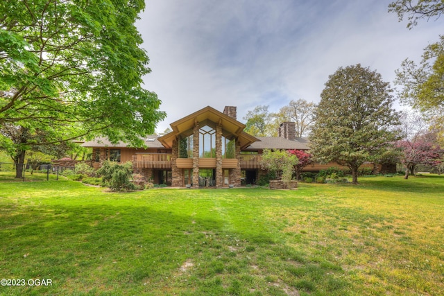 rear view of house featuring stone siding, a chimney, a lawn, and a wooden deck