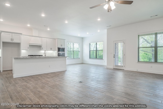 kitchen with white cabinetry, light stone counters, light hardwood / wood-style floors, stainless steel appliances, and a center island with sink