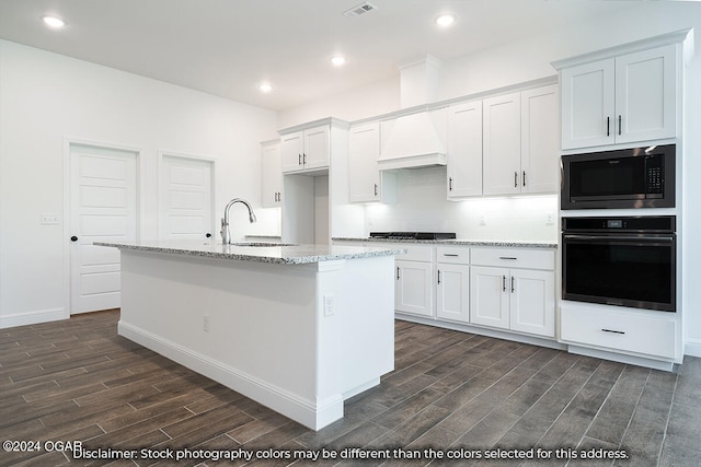 kitchen with built in microwave, white cabinetry, wall oven, and an island with sink