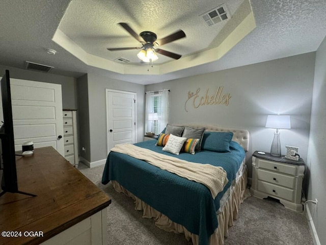 carpeted bedroom featuring a textured ceiling, ceiling fan, and a raised ceiling