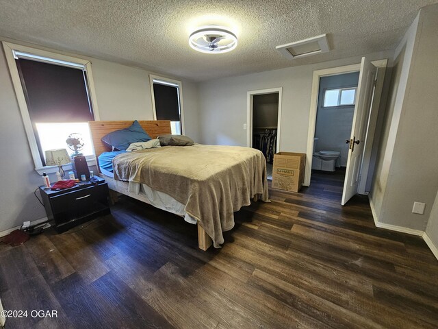 bedroom featuring dark wood-type flooring, a textured ceiling, ensuite bathroom, a closet, and a walk in closet