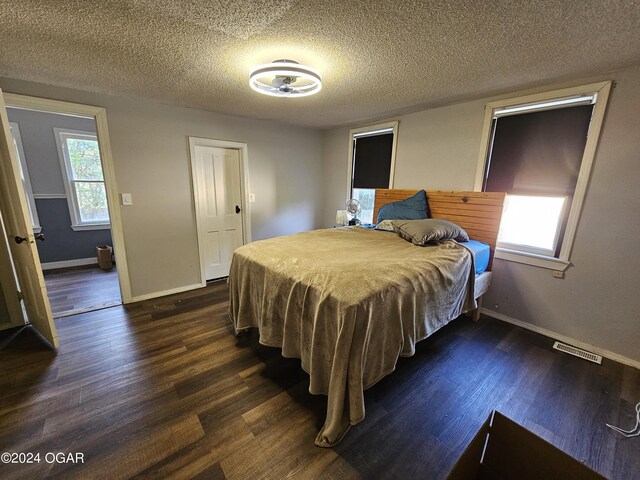 bedroom featuring a textured ceiling, dark wood-type flooring, and multiple windows