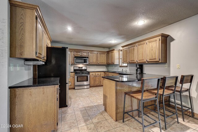 kitchen featuring light tile patterned floors, appliances with stainless steel finishes, a kitchen breakfast bar, a peninsula, and a textured ceiling