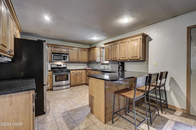 kitchen with appliances with stainless steel finishes, light tile patterned flooring, a textured ceiling, a peninsula, and a kitchen breakfast bar