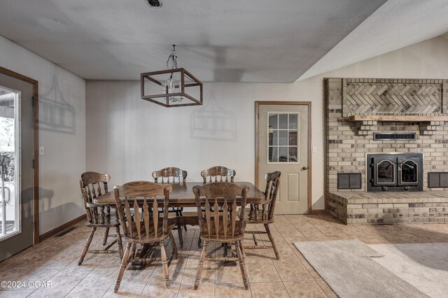 dining space featuring visible vents, baseboards, tile patterned floors, an inviting chandelier, and a brick fireplace