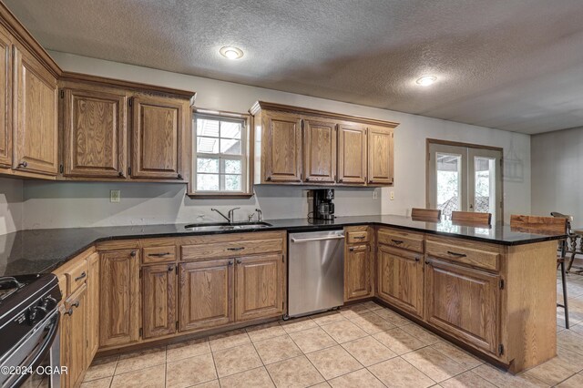 kitchen with light tile patterned floors, appliances with stainless steel finishes, brown cabinetry, a sink, and a peninsula