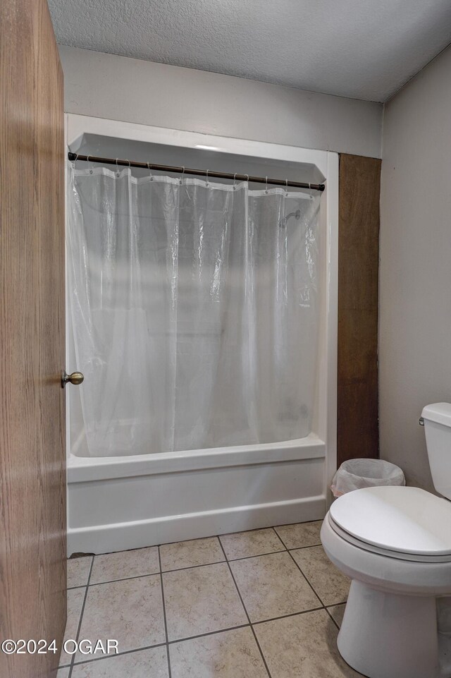 full bath featuring tile patterned flooring, shower / tub combo with curtain, a textured ceiling, and toilet