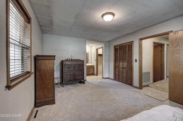 carpeted bedroom with a textured ceiling, ensuite bath, visible vents, and baseboards