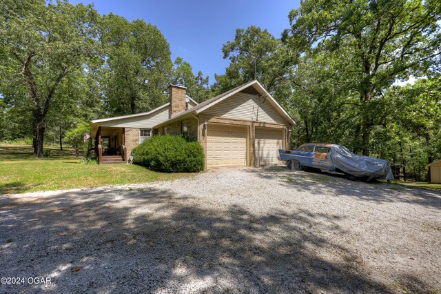 view of home's exterior with a garage, brick siding, driveway, a yard, and a chimney